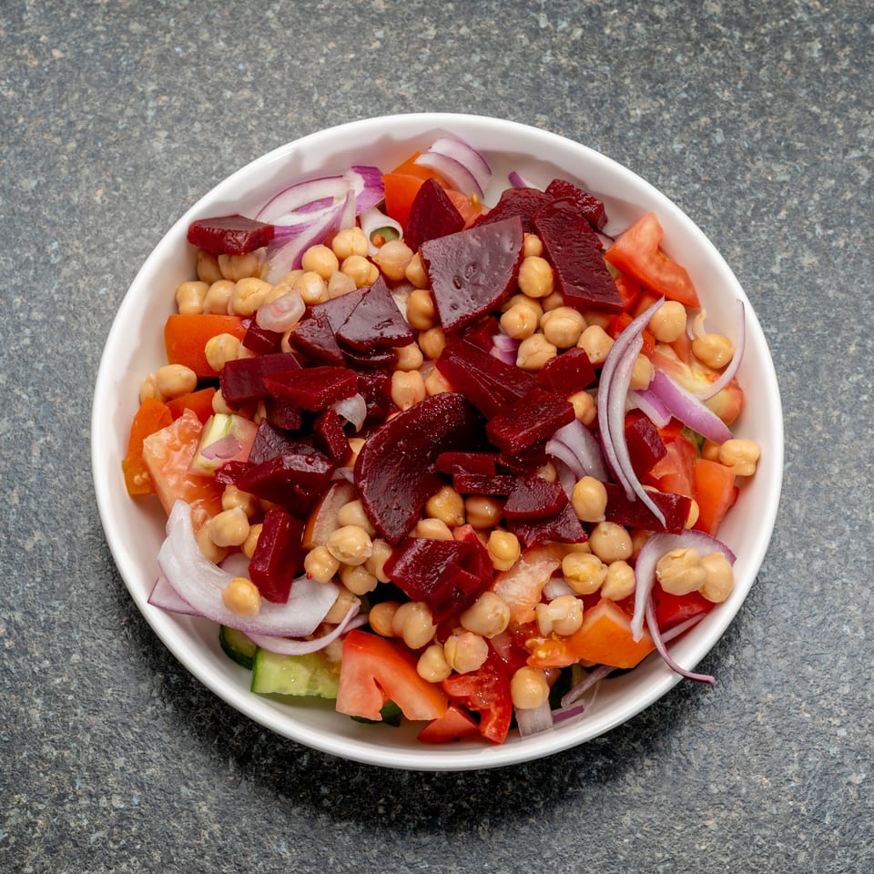 A white bowl filled with a colorful salad of chickpeas, diced beets, red onions, and tomatoes.