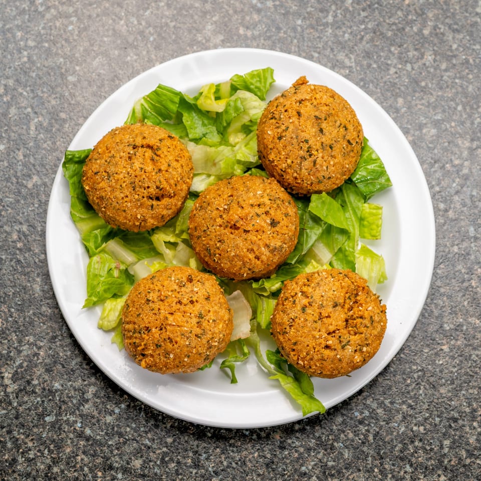 Five golden-brown falafel balls rest on a bed of fresh green lettuce on a white plate.