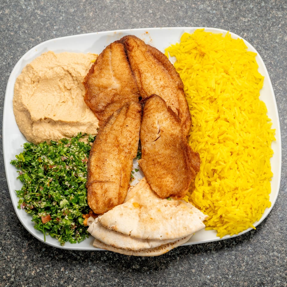 A white platter holds fried fish, yellow rice, hummus, tabbouleh, and pita bread.