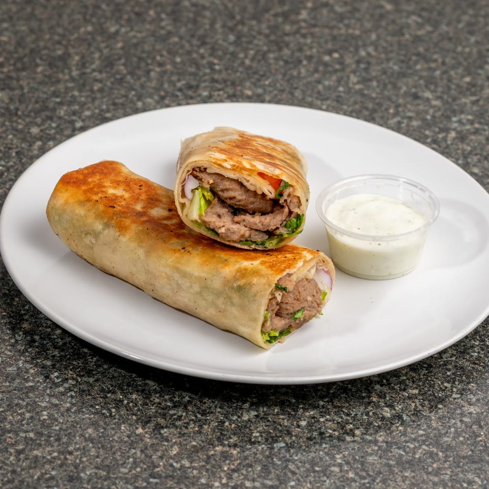 Two grilled meat wraps, one cut in half, with a side of white sauce on a white plate.