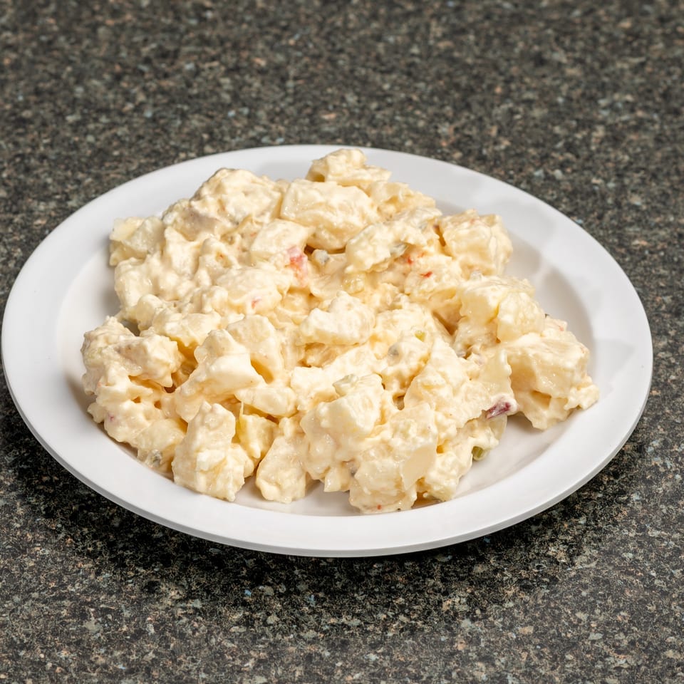 Creamy potato salad with diced potatoes and red specks, served on a white plate.
