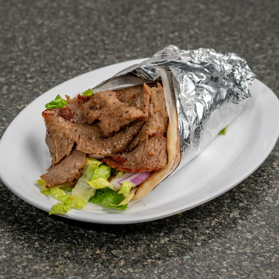 A gyro sandwich with meat, lettuce, and red onion, partially wrapped in foil on a white plate.