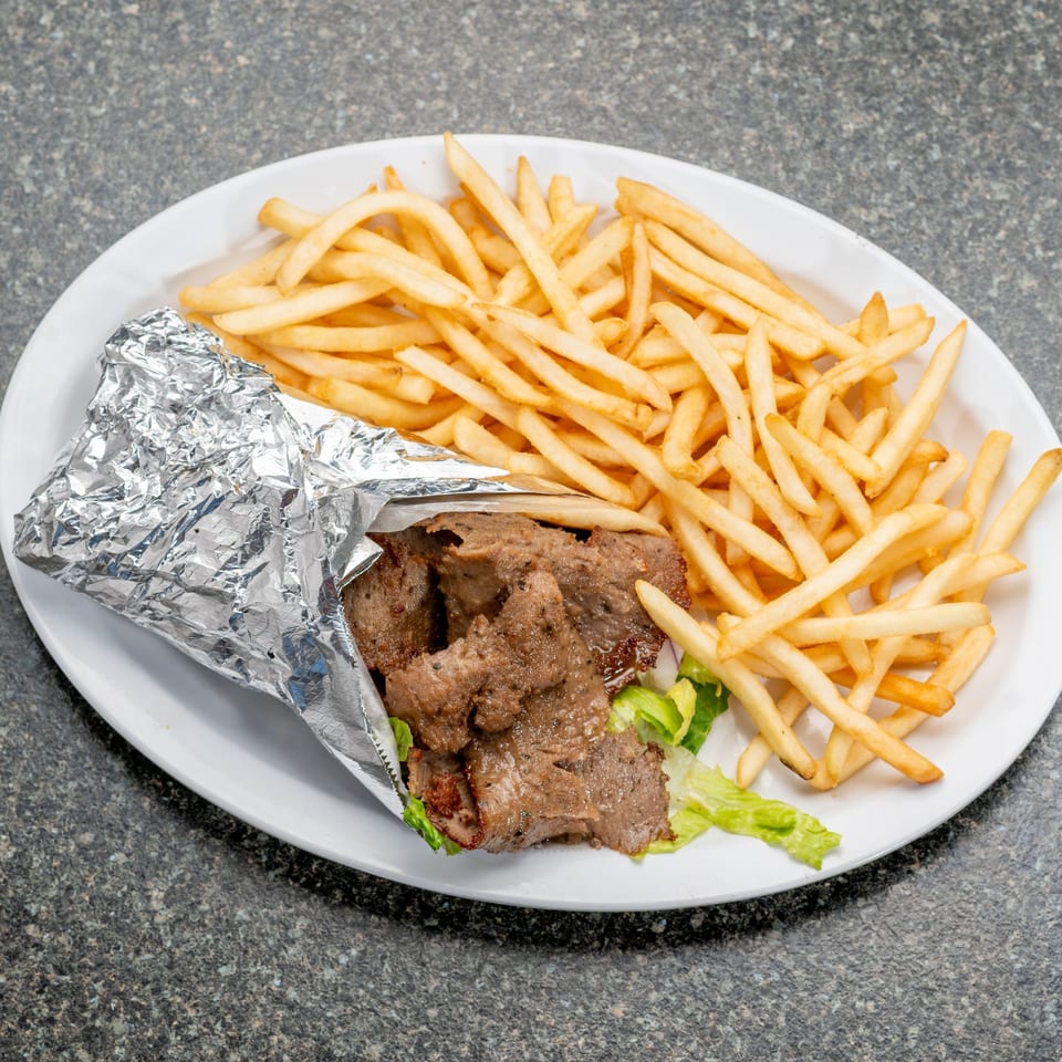 Gyro meat in foil with lettuce and fries on a white plate.