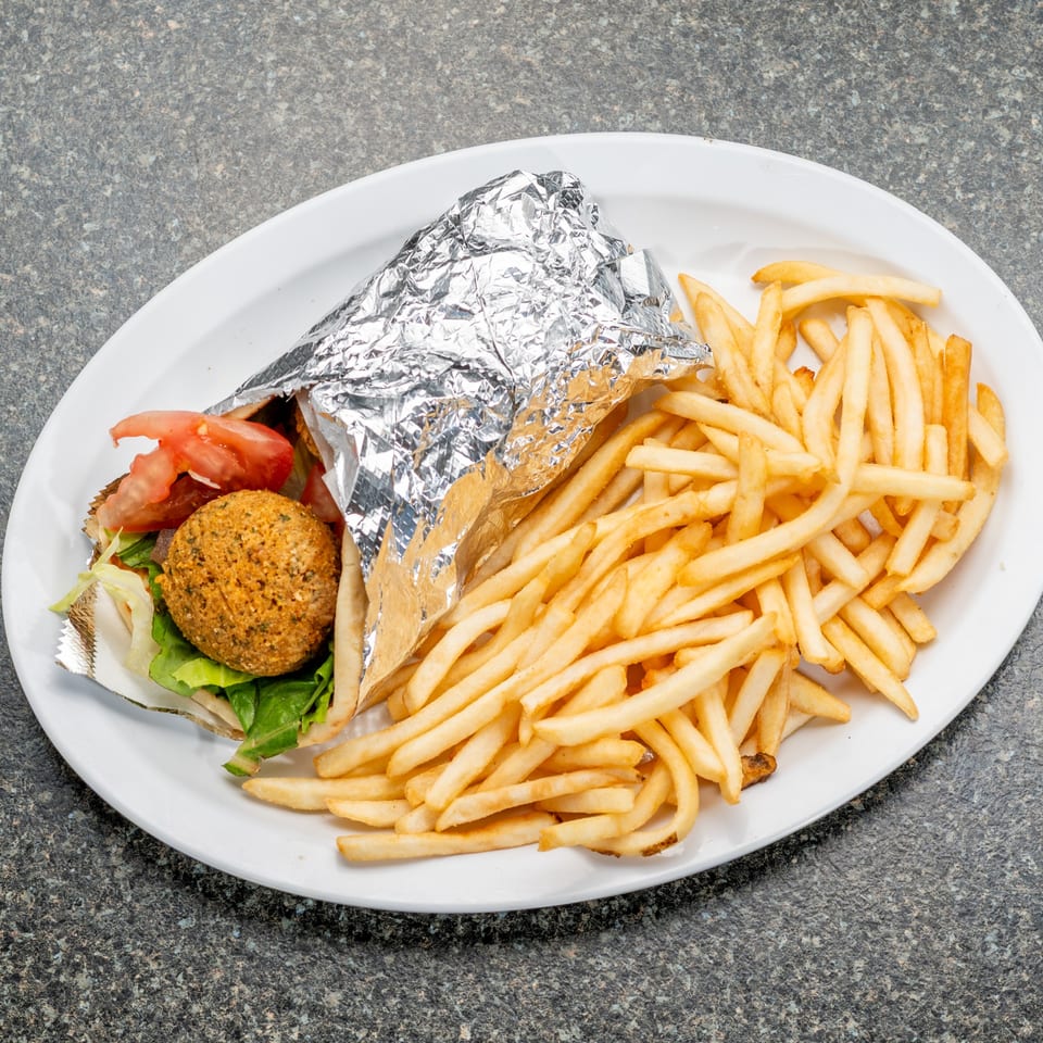 Falafel wrap with lettuce and tomato, partially wrapped in foil, served with a side of french fries.