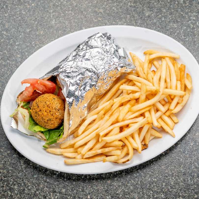 Falafel wrap with lettuce and tomato, partially wrapped in foil, served with a side of french fries.