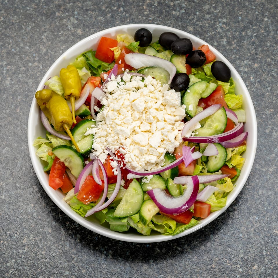 A vibrant Greek salad with lettuce, tomatoes, cucumbers, red onions, olives, feta, and pepperoncini.