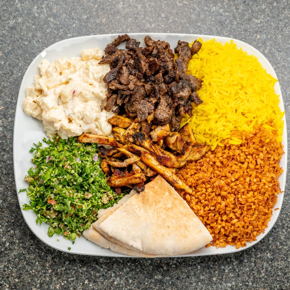 A platter with beef and chicken shawarma, yellow rice, bulgur, tabbouleh, macaroni salad, and pita bread.