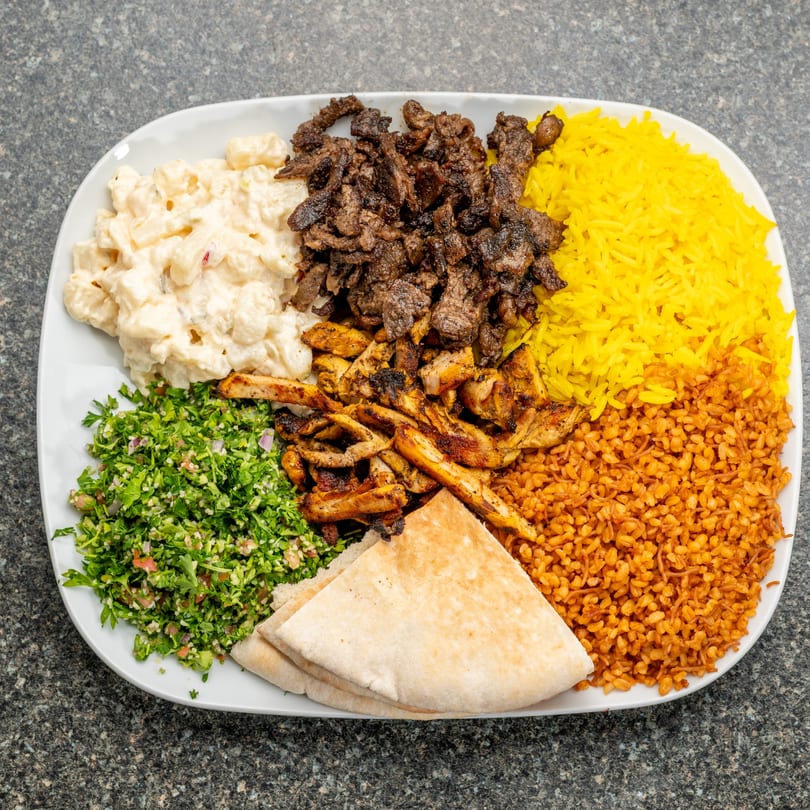 A platter with beef and chicken shawarma, yellow rice, bulgur, tabbouleh, macaroni salad, and pita bread.