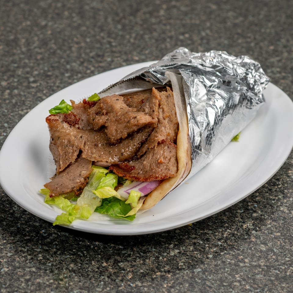 A gyro sandwich, partially wrapped in foil, filled with meat, lettuce, and red onion on a white plate.