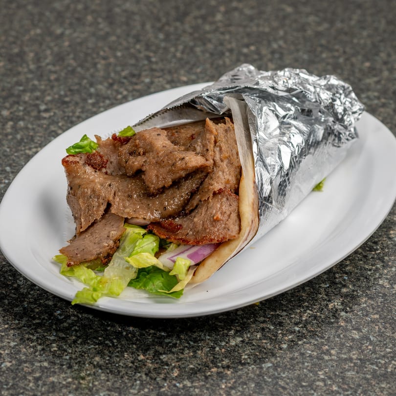 A gyro sandwich, partially wrapped in foil, filled with meat, lettuce, and red onion on a white plate.